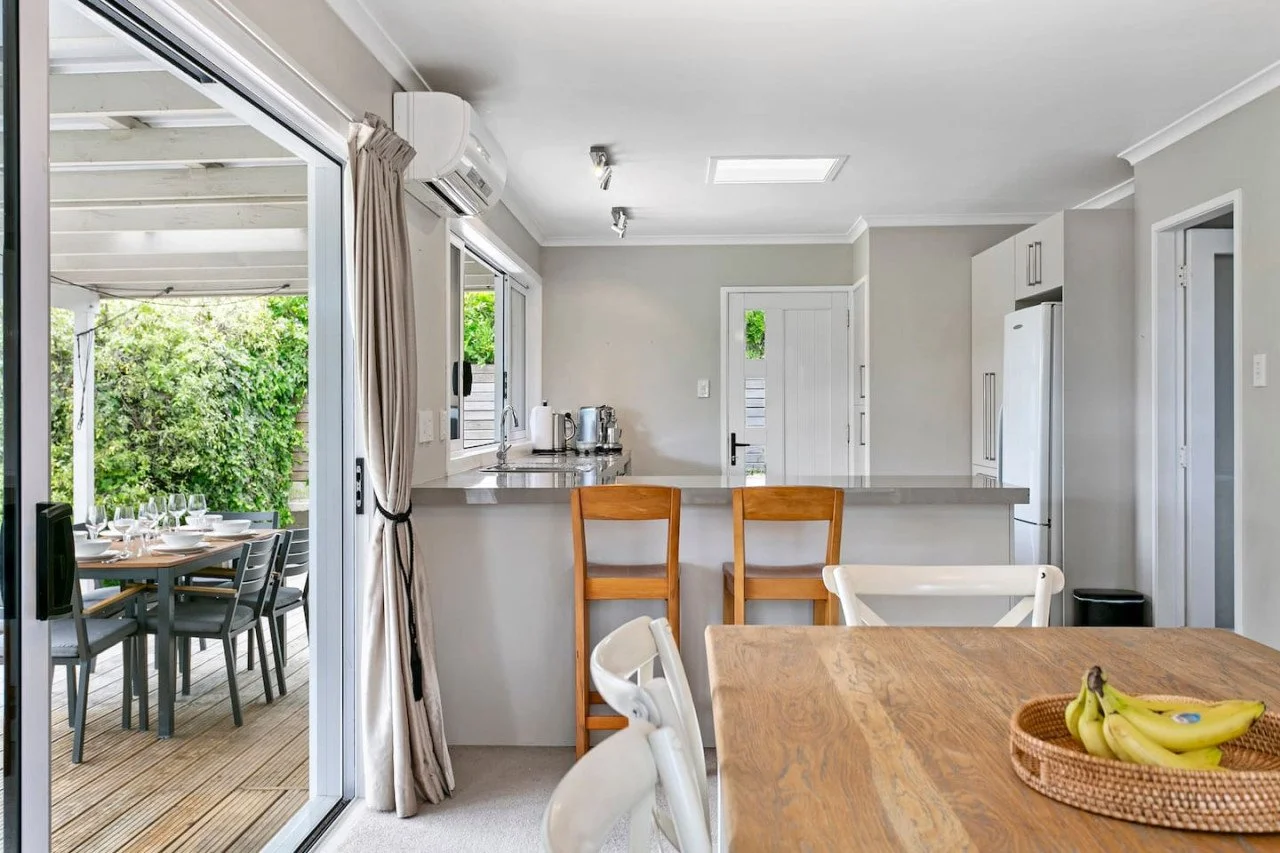 Open kitchen and dining area with sliding glass door leading to patio, outdoor dining table, and greenery outside.