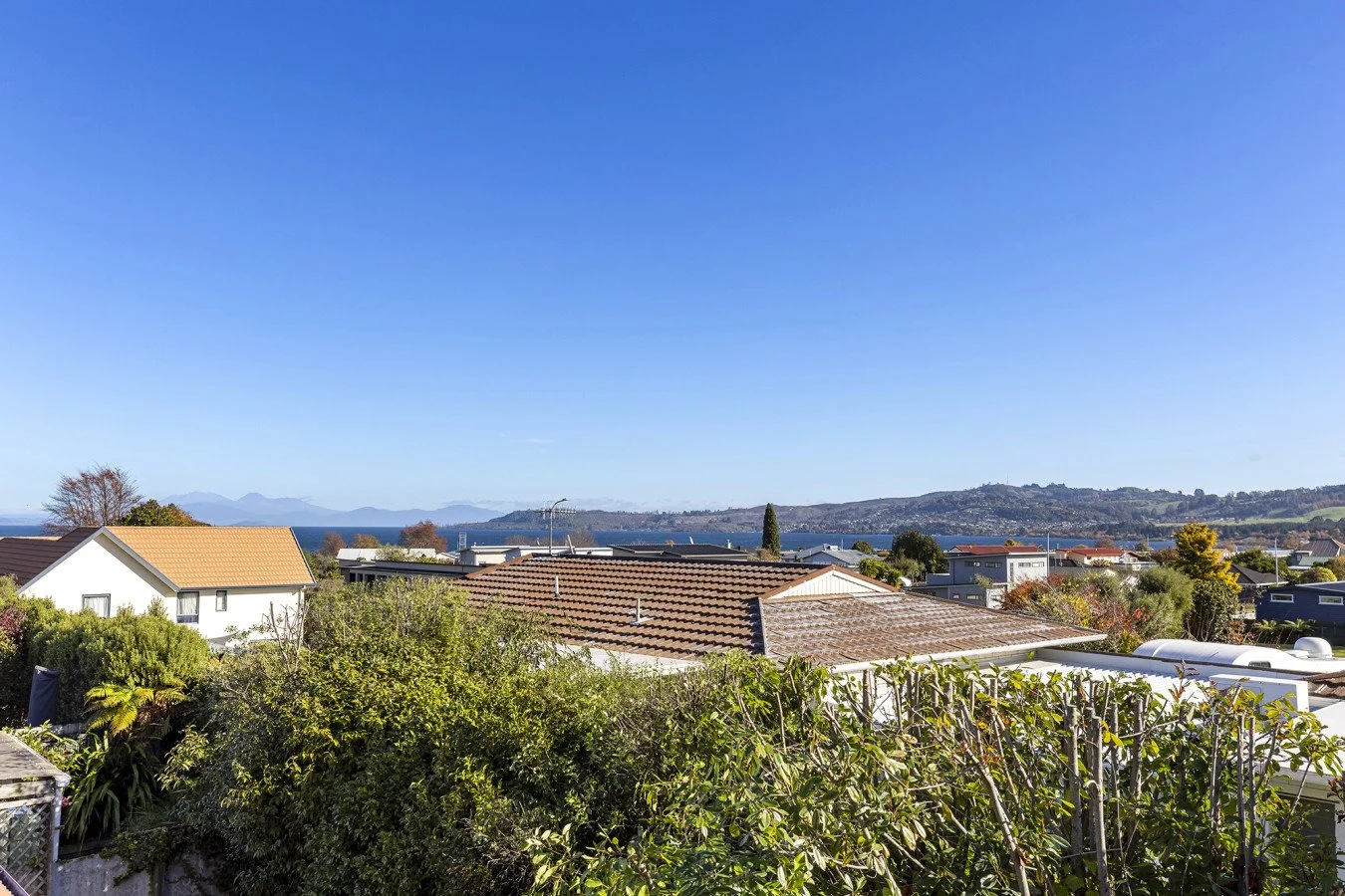 A scenic view of a residential neighborhood with rooftops, trees, and distant hills under a clear blue sky.