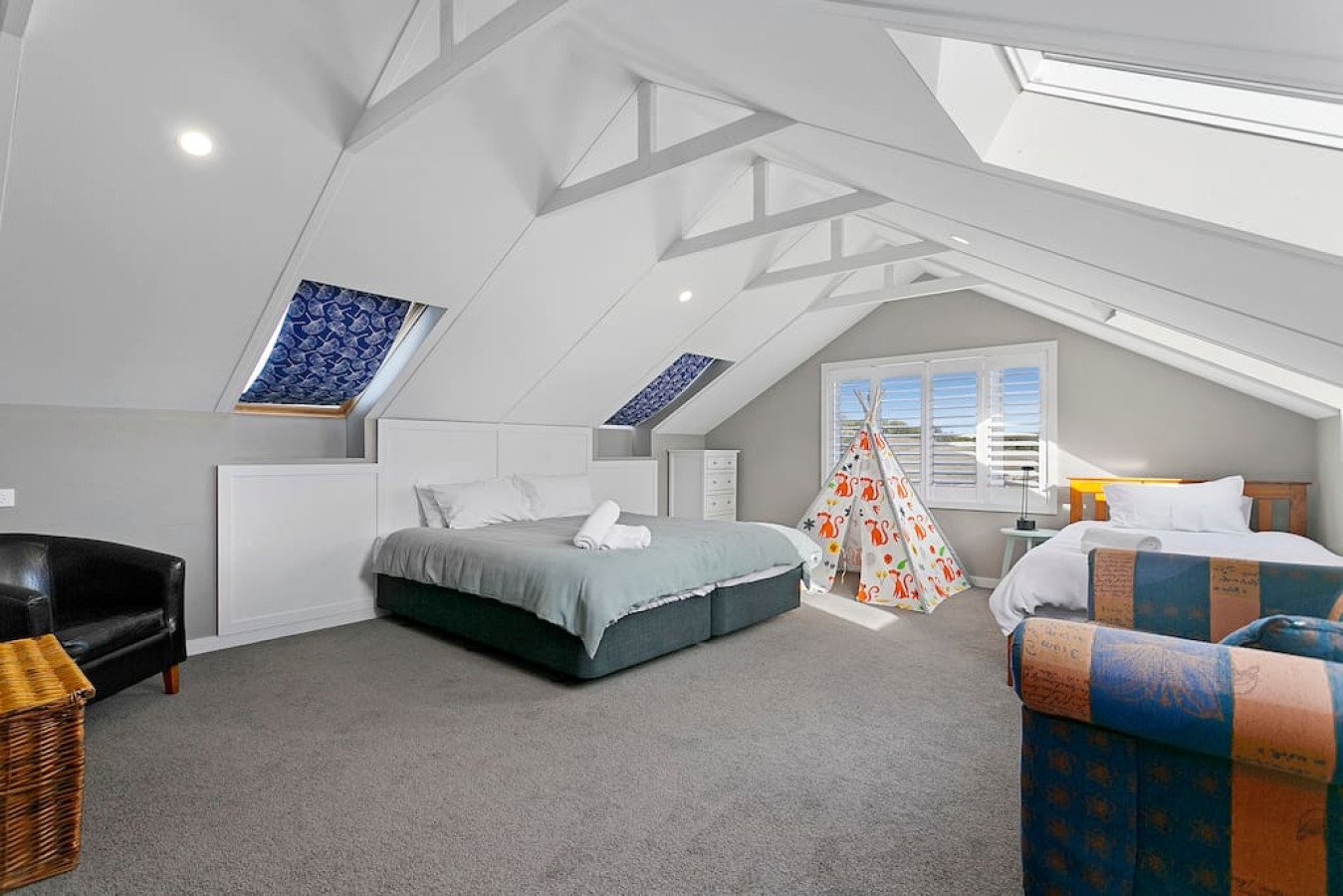 Spacious attic bedroom with two beds, a tent, window, skylights, and comfortable seating.