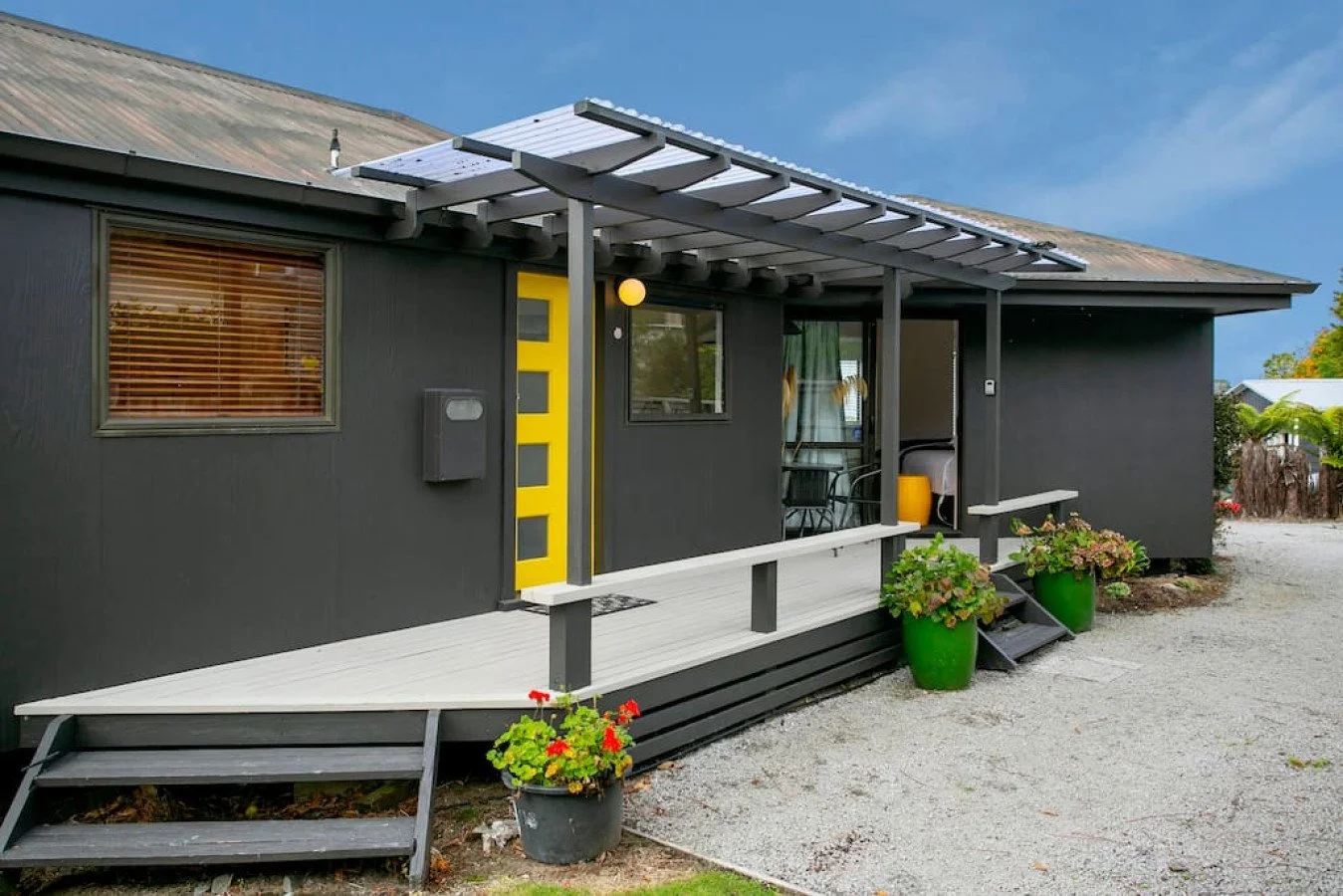 A black house with a small porch, yellow front door, and potted plants outside. The house has a sloped roof with newly installed solar panels.