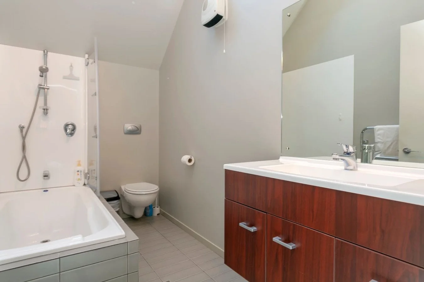 A bathroom with a bathtub, toilet, and a wooden vanity with a sink and a large mirror.