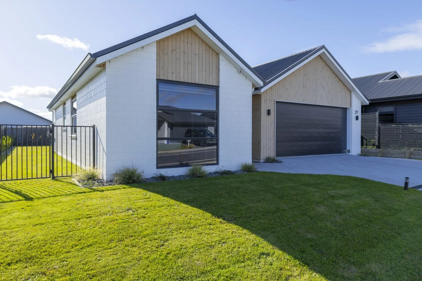 Modern house with white brick and wooden exterior, large garage door, and well-maintained lawn under a blue sky.