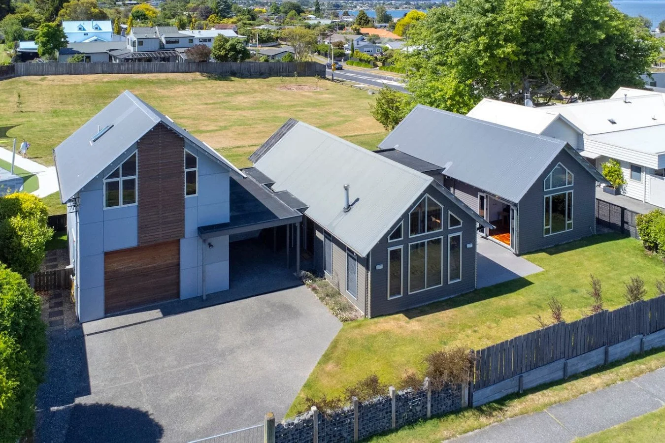 A modern house with multiple gabled roofs, large windows, and a driveway, located in a suburban neighborhood with green lawns and trees.