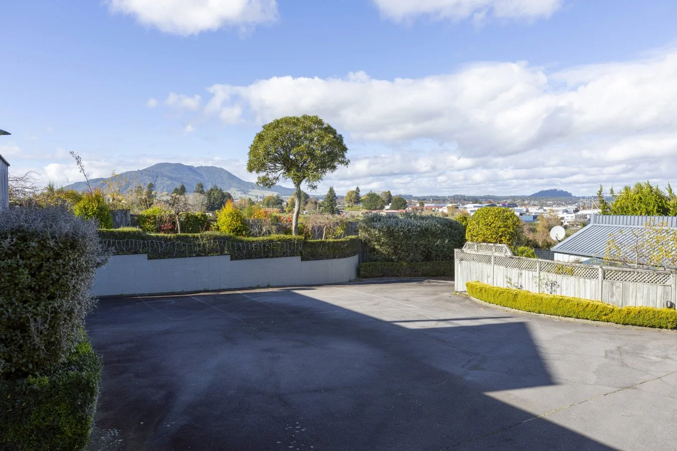 Empty parking lot with a view of distant mountains, trees, and a partly cloudy sky.