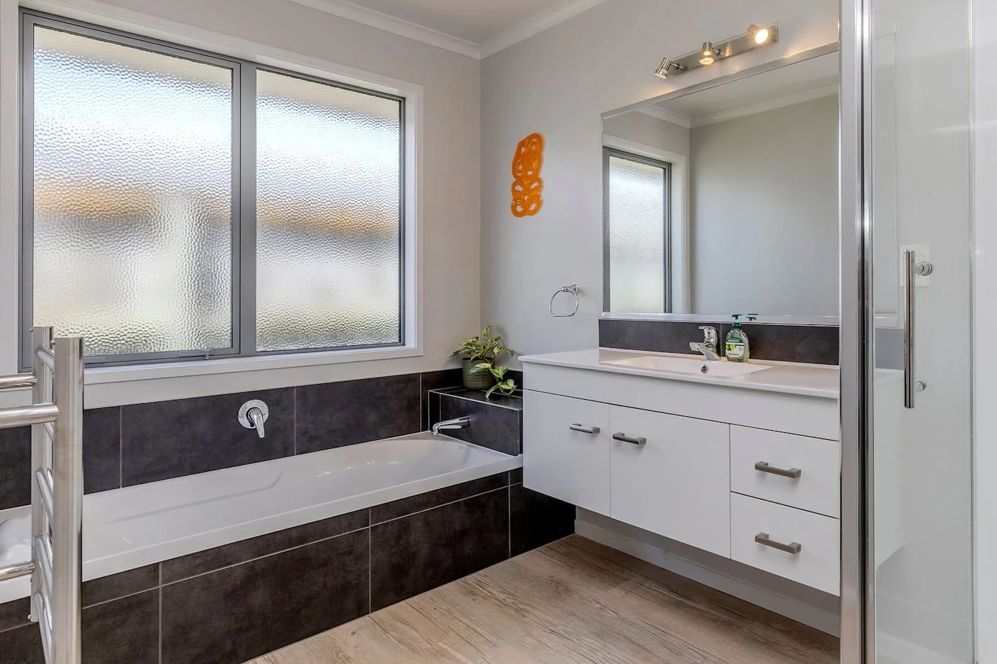 Modern bathroom with frosted windows, a built-in bathtub, white vanity with drawers, large mirror, and shower stall