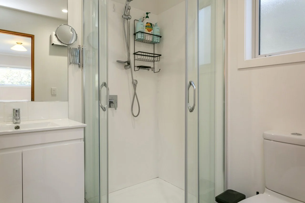 Bathroom with a shower stall, white sink with cabinet, and white toilet, with a window and mirror.