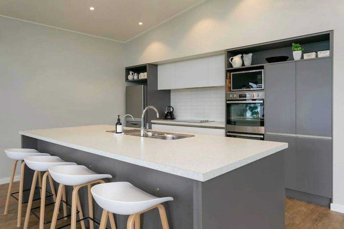 Modern kitchen with gray cabinetry, white countertop island, stainless steel appliances, bar stools, and minimal decor.