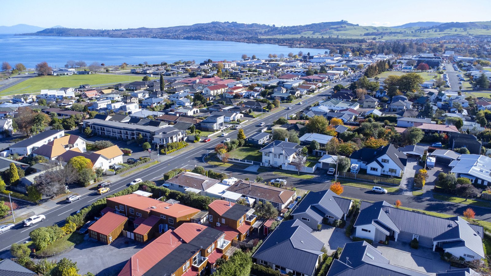 Aerial view of a residential neighborhood near a large body of water, with houses, streets, and green trees.