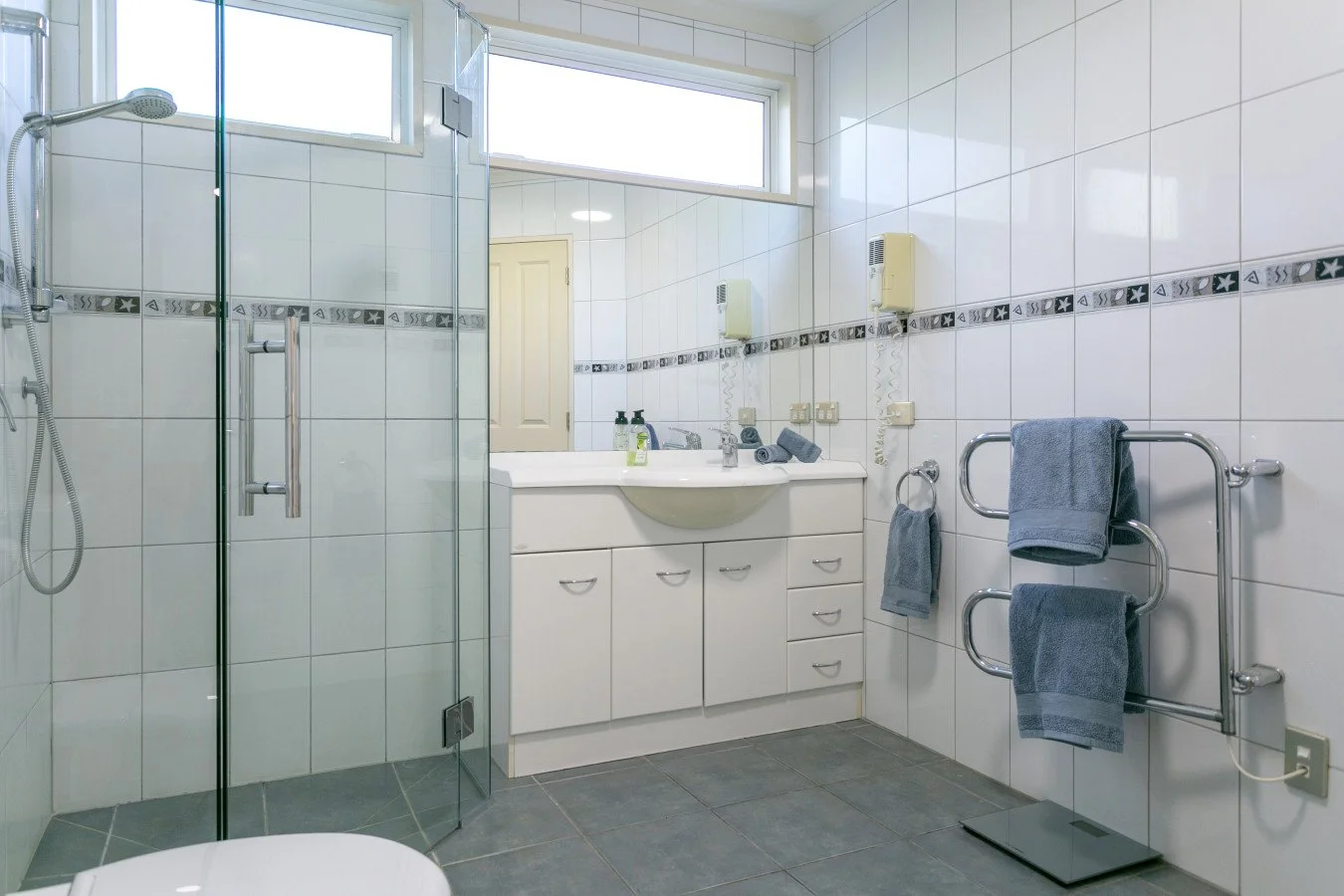 A clean, modern bathroom with a shower enclosure, a sink with a mirror, and towel racks with blue towels.