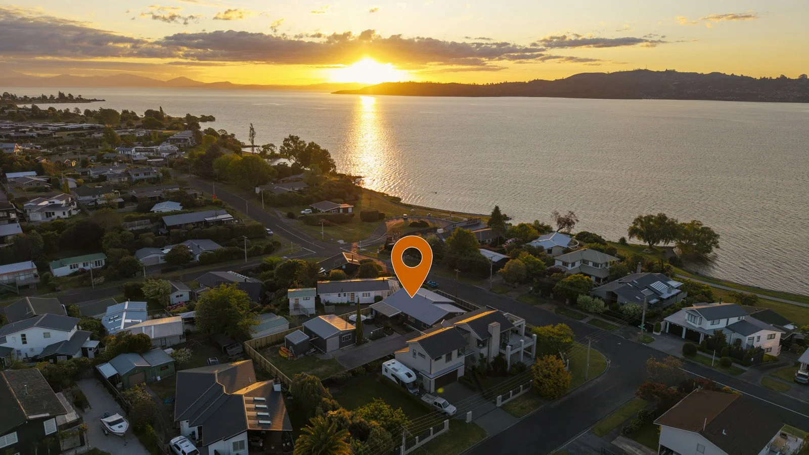 Aerial view of a neighborhood near a large body of water at sunset, with an orange location pin marking a house.