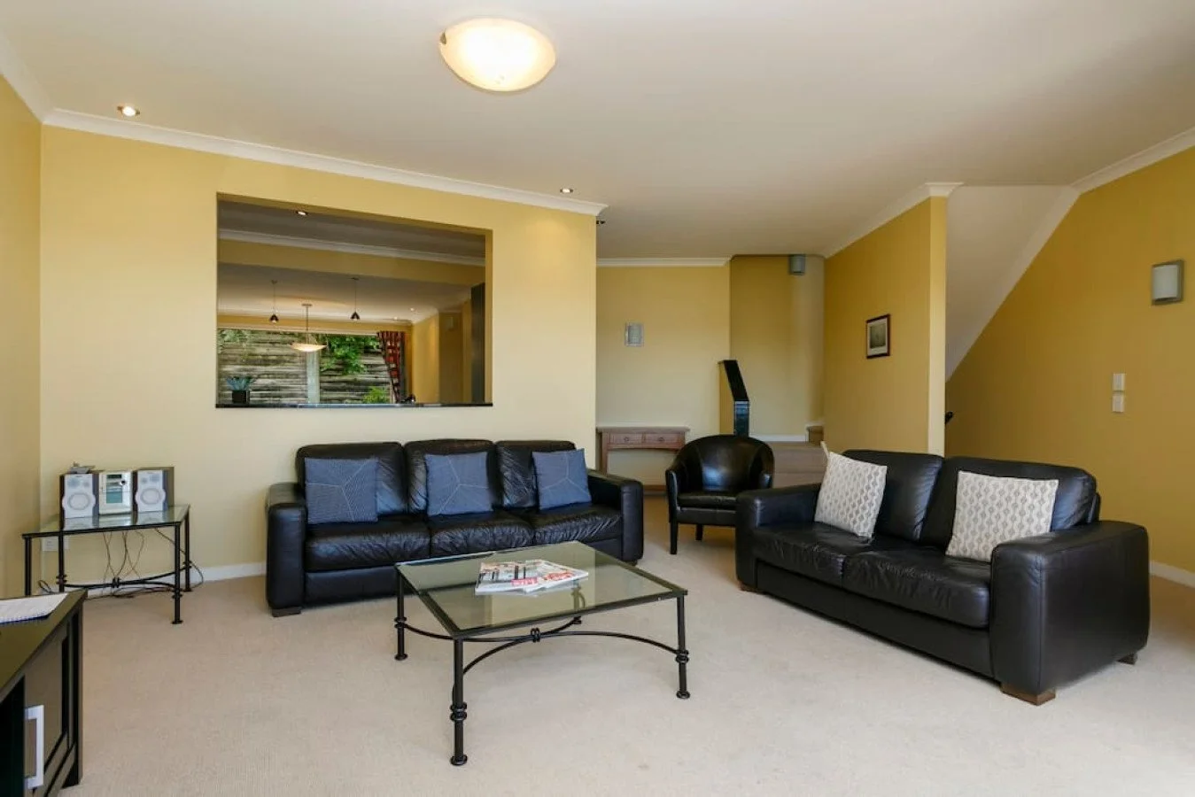 Living room with yellow walls, black leather sofas, glass coffee table, and decorative pillows.