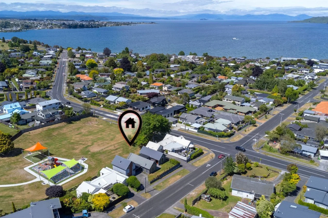 Aerial view of a coastal residential neighborhood with houses, roads, and a large body of water in the background, with a marker indicating a specific house or property.