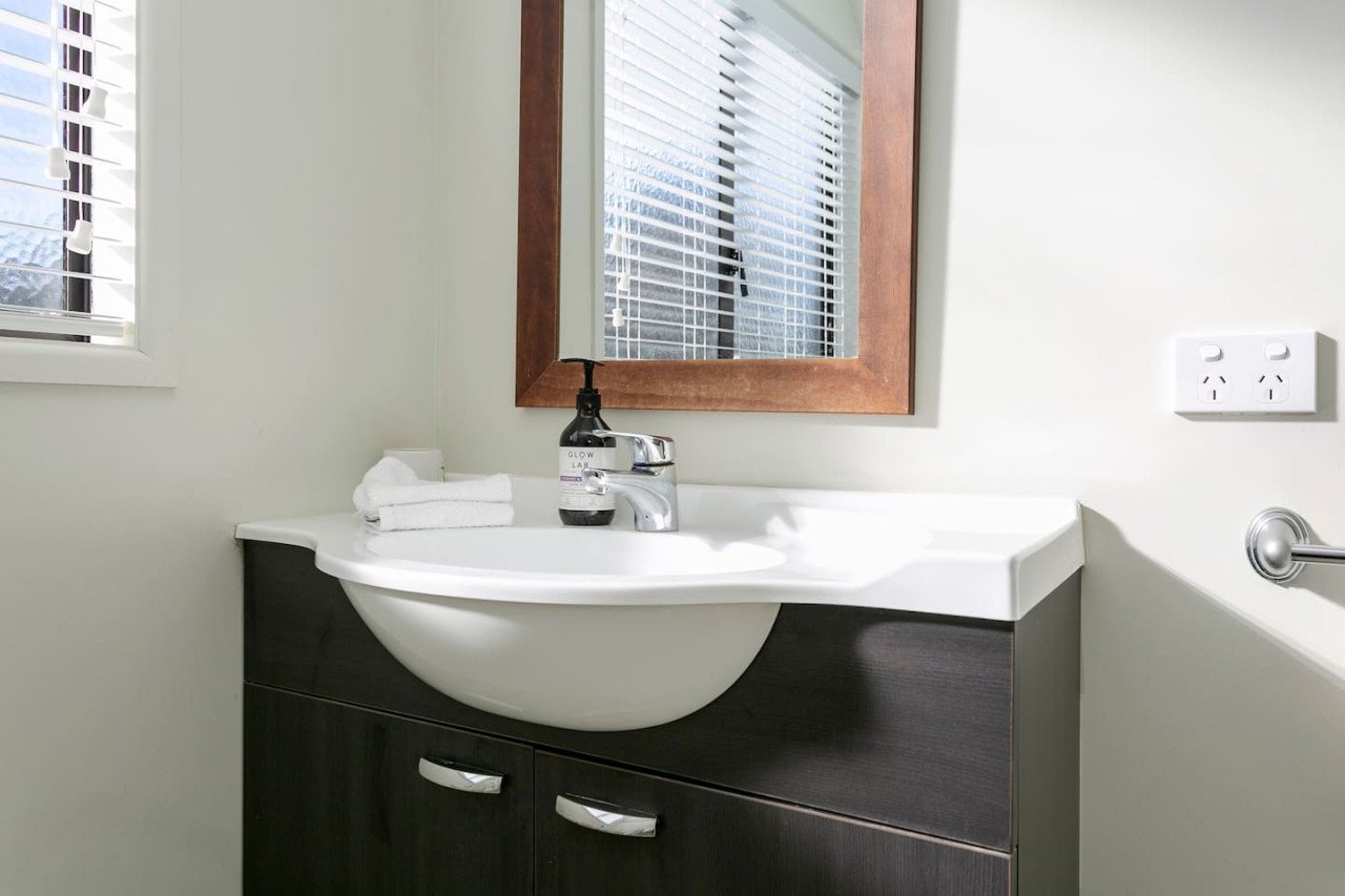 Bathroom sink with mirror, faucet, soap dispenser, folded towels, electrical outlet, and window with blinds.