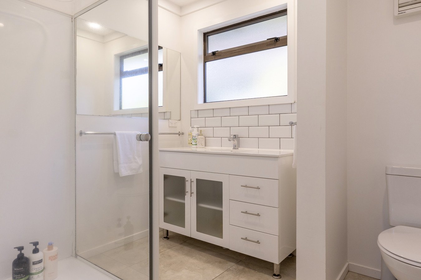 A small bathroom with a walk-in shower, a white vanity with a sink, and frosted windows.