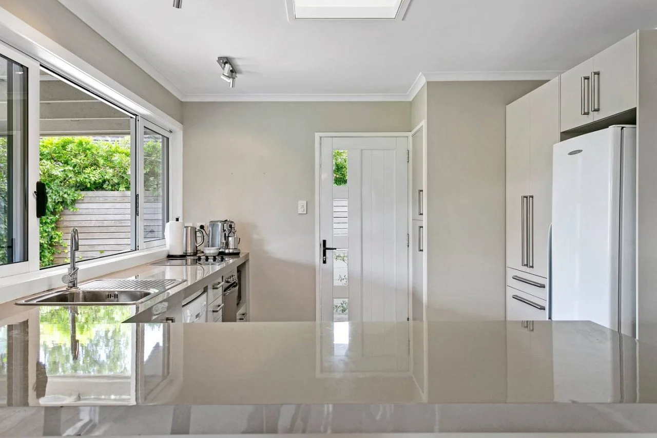 Modern kitchen with white cabinets and a large window overlooking greenery, with appliances and a countertop.
