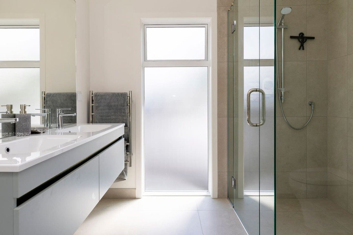 Modern bathroom with a double sink vanity, frosted glass door, and a walk-in shower with glass enclosure.
