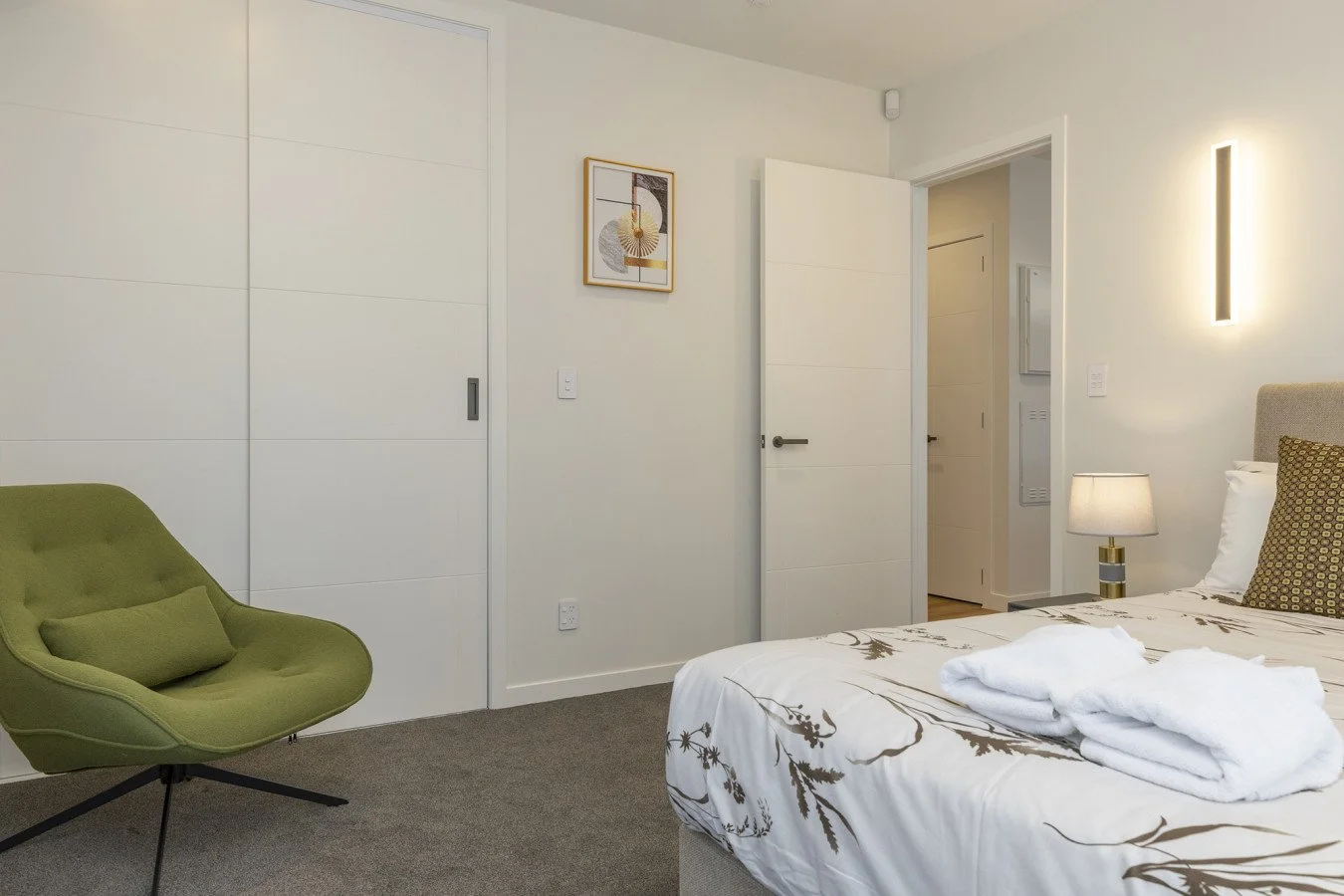 A bedroom with a bed, a lamp, a green chair, and a framed artwork on the wall.