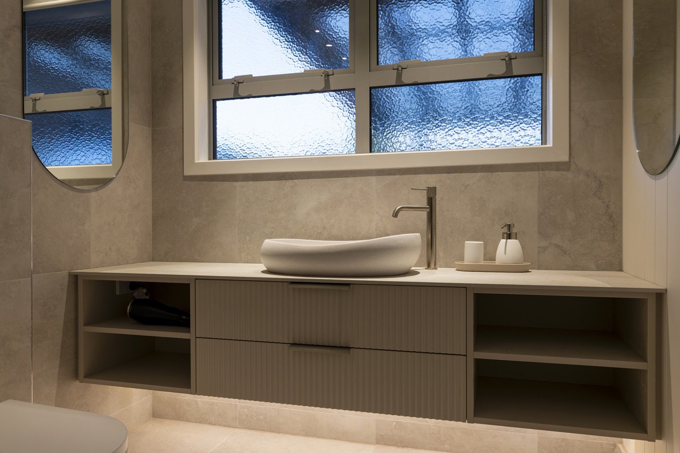 Modern bathroom vanity with a vessel sink, faucet, mirror, and window with textured glass.