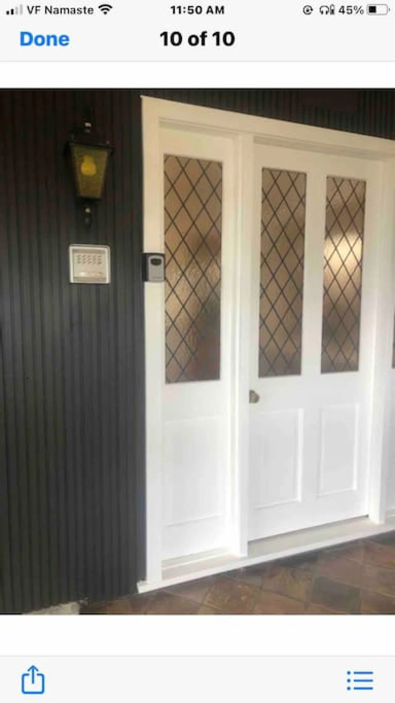 Image of a white door with frosted glass panels and diamond-patterned wire mesh, next to a black textured wall with a yellow light fixture and a doorbell camera.