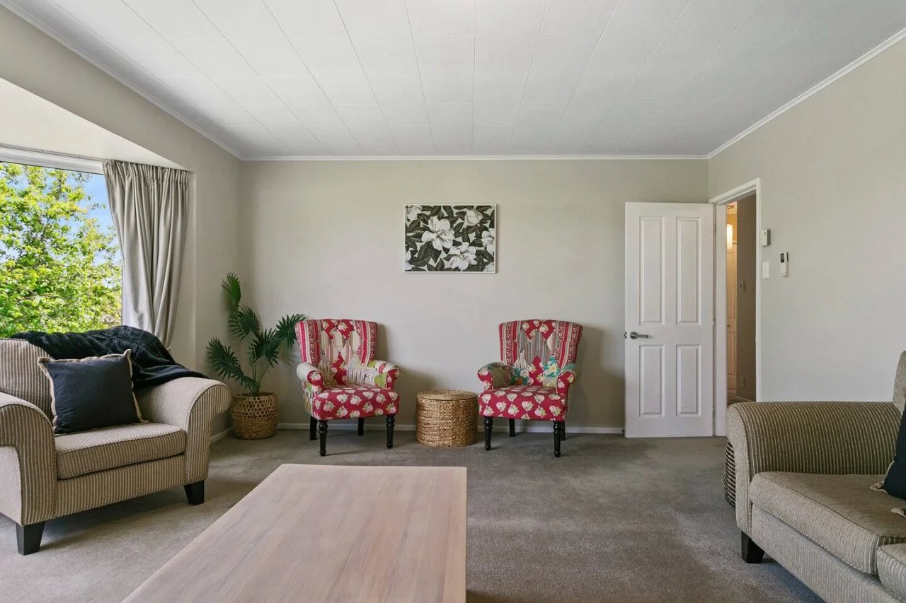 Living room with beige sofas, red patterned armchairs, a potted plant, and a window with curtains.