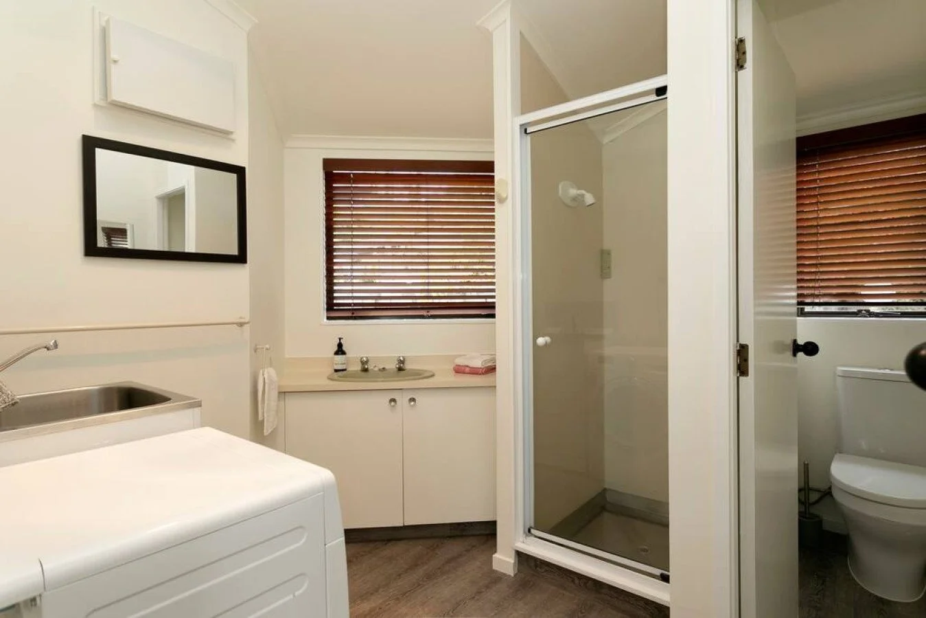 Bathroom with washing machine, sink, mirror, toilet, walk-in shower, windows with wooden blinds