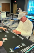 Two people playing a card game at a black table in a room with blue curtains and wooden walls.