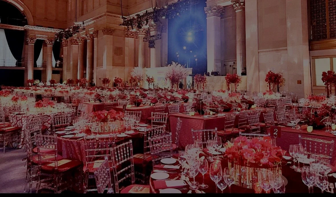 Elegant banquet hall with round tables, floral centerpieces, chairs, and a stage with blue lighting.