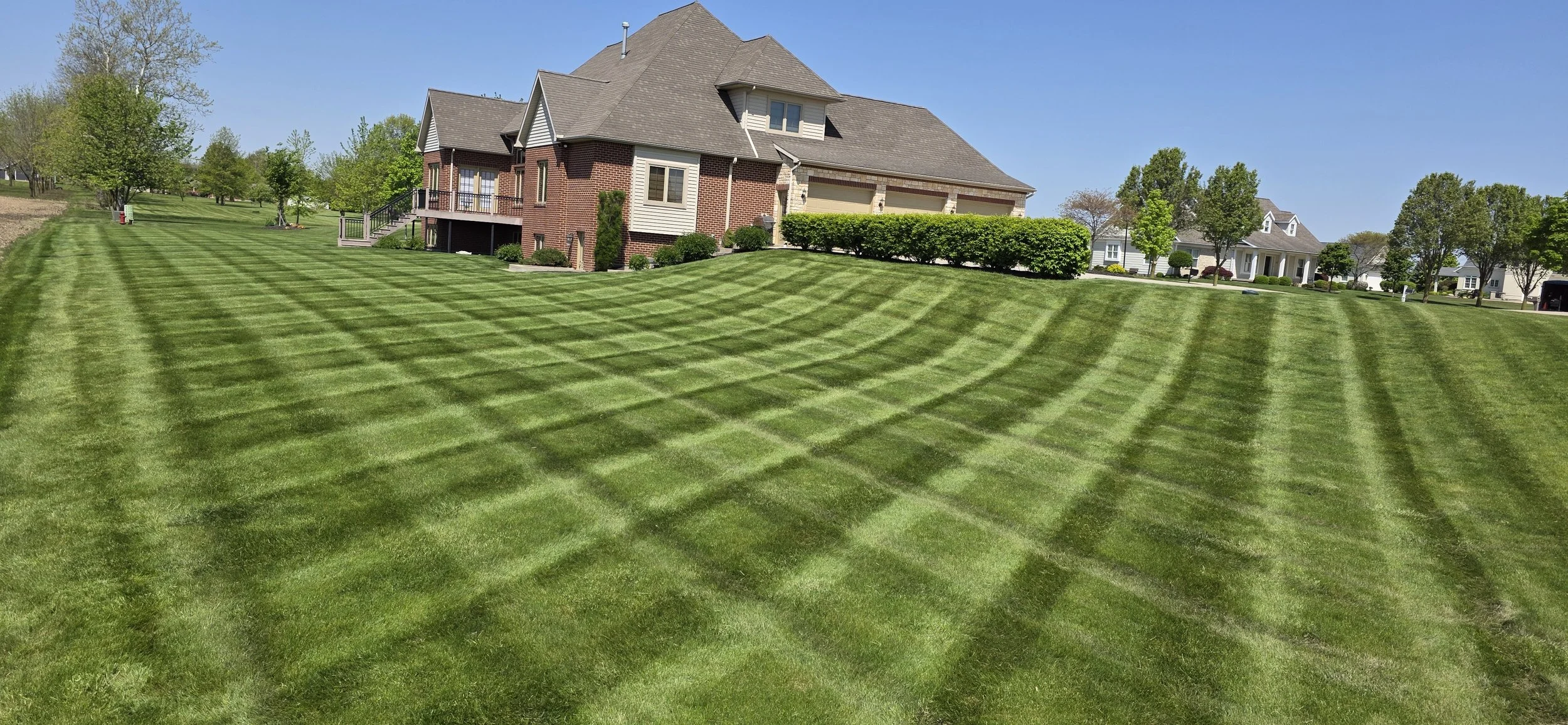 A house with a large, well-maintained lawn featuring a checkerboard pattern of freshly mowed grass on a sunny day.