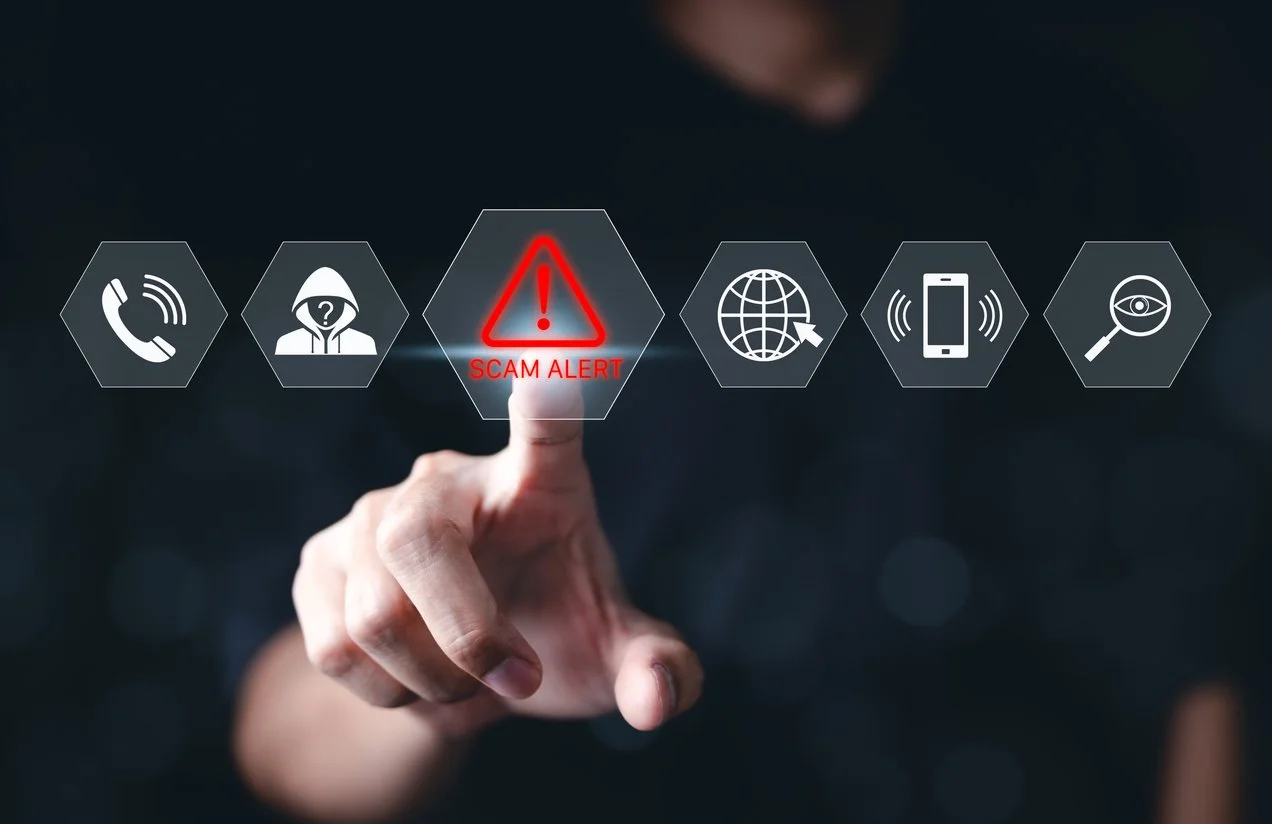 Person touching a virtual screen displaying icons, including a red warning sign with an exclamation mark and 'SCAM ALERT' message, indicating a scam warning.