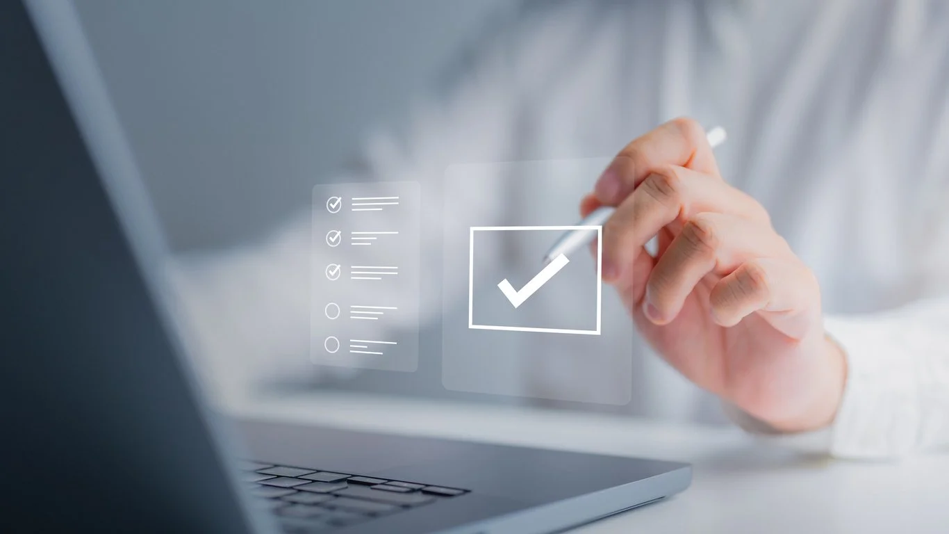 Person using a stylus to check off items on a digital touch screen interface above a laptop.