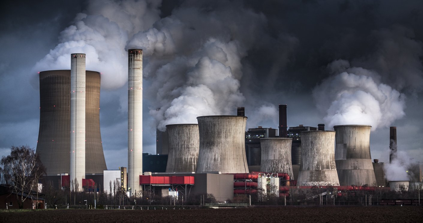 An industrial power plant with multiple cooling towers and smokestacks emitting large amounts of smoke and steam.