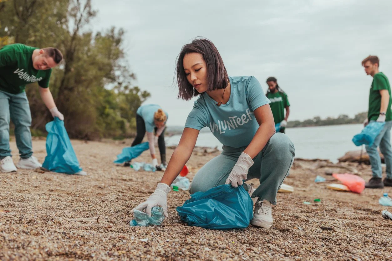 Group of volunteers cleaning up trash on a beach, picking up plastic bottles and debris.