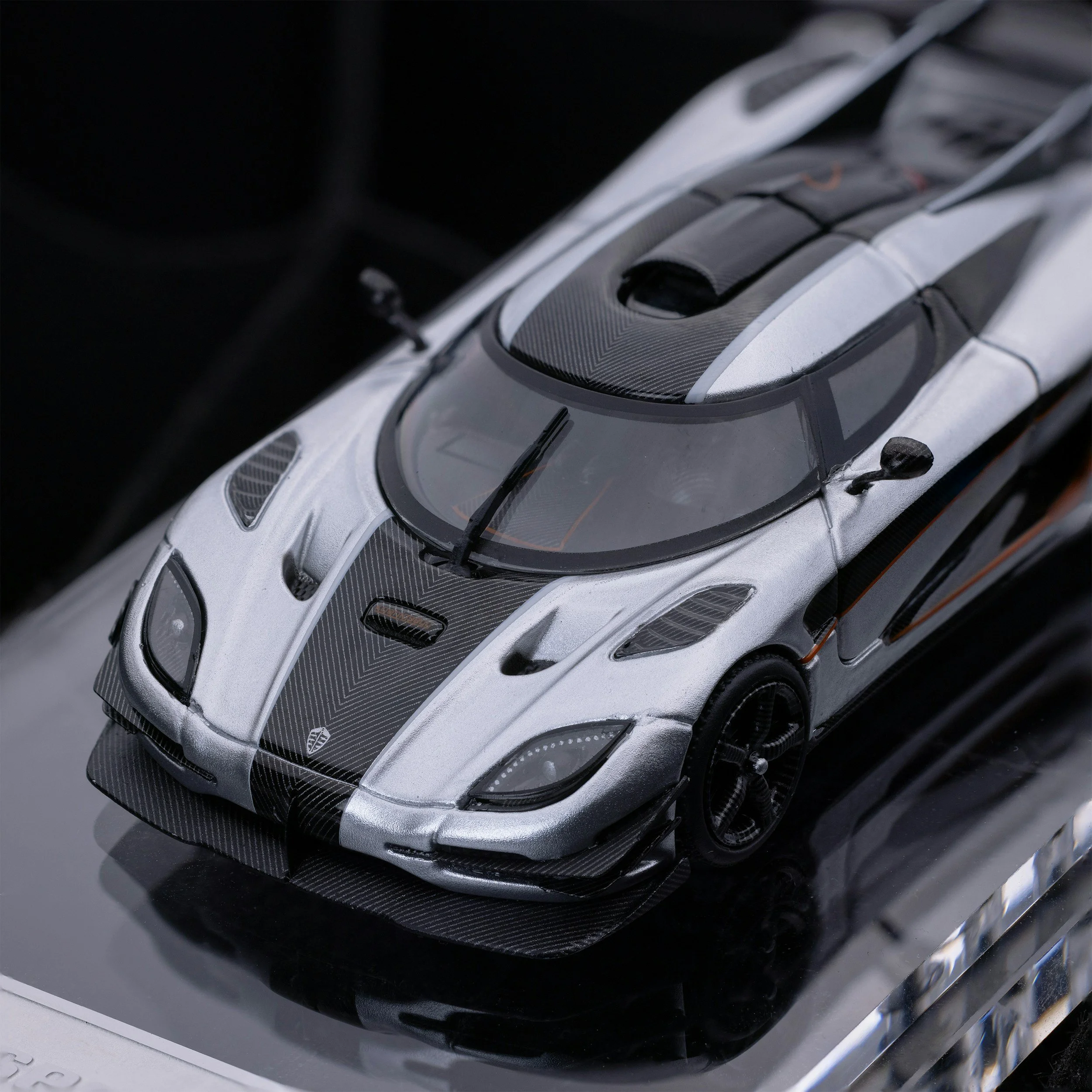 A detailed model of a silver and black sports car with carbon fiber accents, showcased on a reflective black surface.