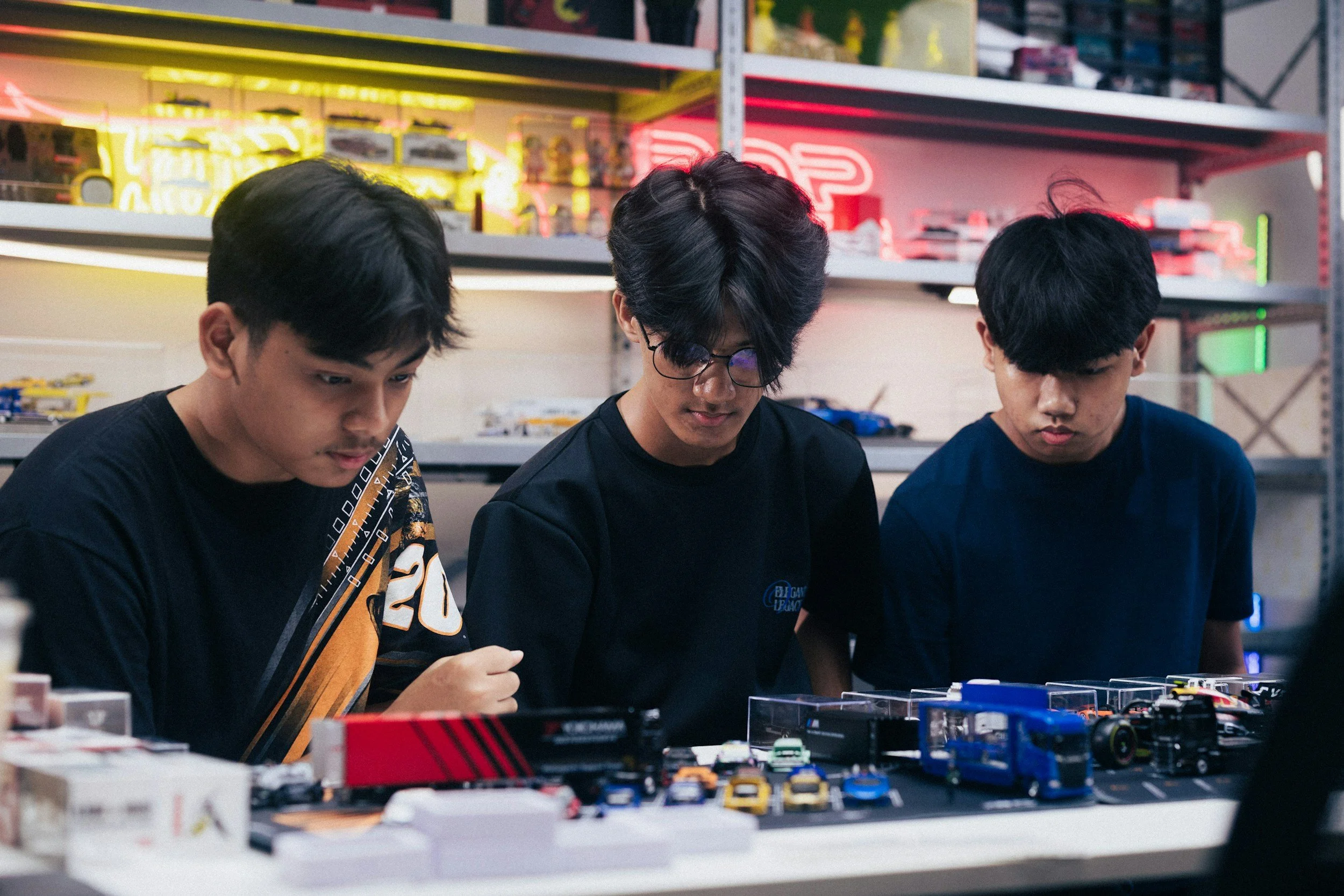 Three young men looking at a collection of model cars on a table in a toy store or hobby shop.