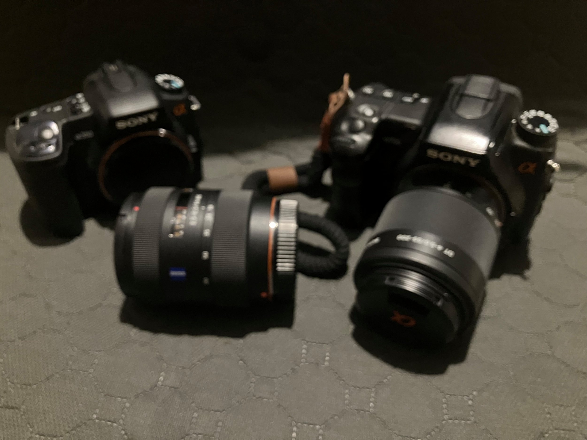 Sony A350 body and Sony A700 with a 55–200mm lens, with a Carl Zeiss 16–80mm lens placed between them on a textured mat.