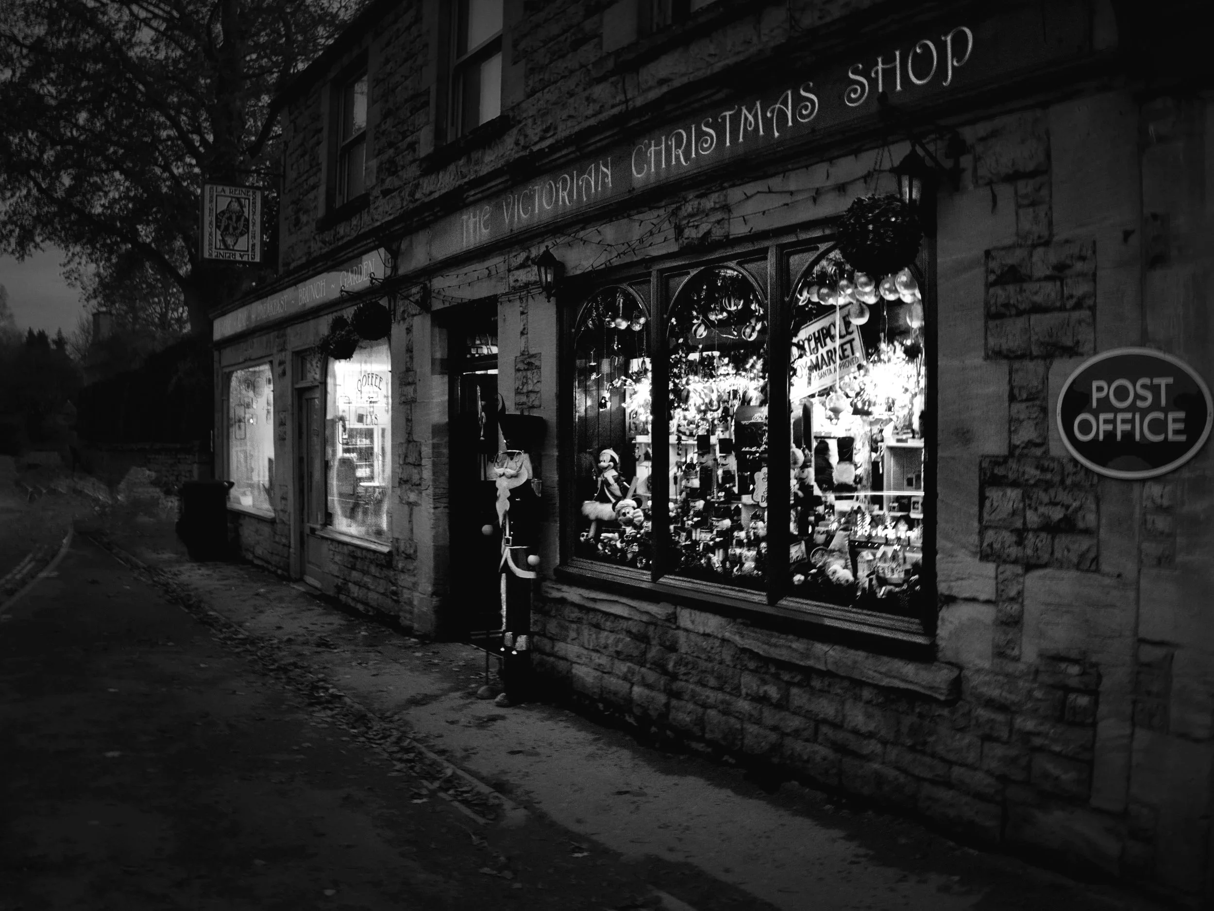 “Evening light glows from the Victorian Christmas Shop in Bourton-on-the-Water, the warm window displays contrasting with the quiet street outside.”