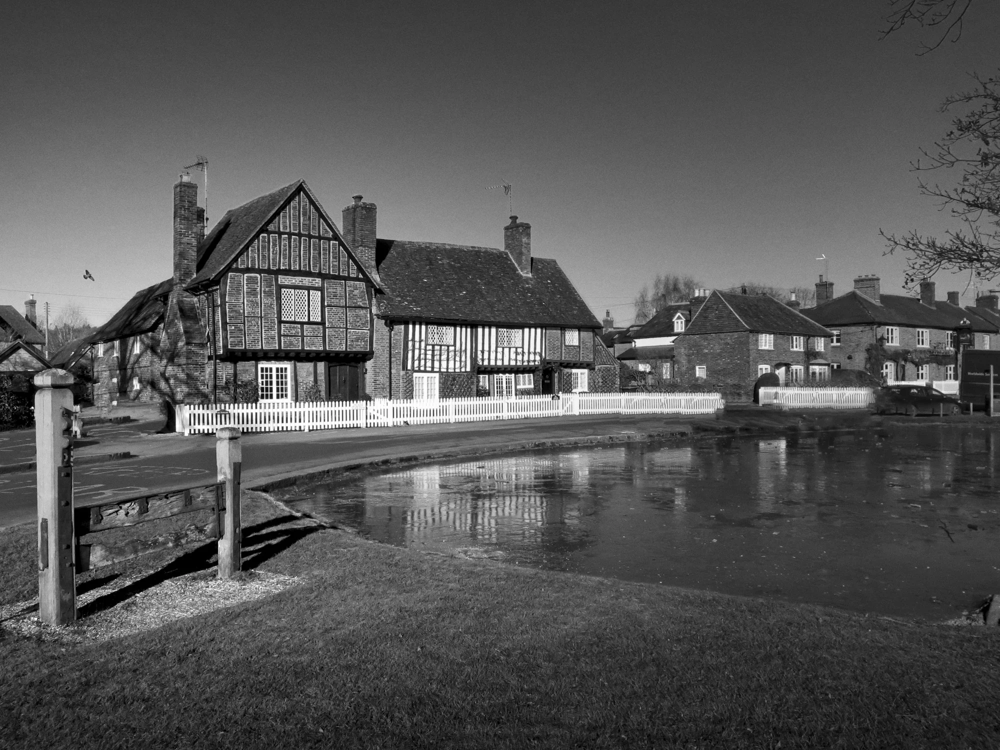 Aldbury village green and pond in winter, Chiltern Hills, Hertfordshire — black and white photograph showing the Tudor timber-framed cottages, original village stocks and frozen pond by Mark Weekes from Walking With Pics