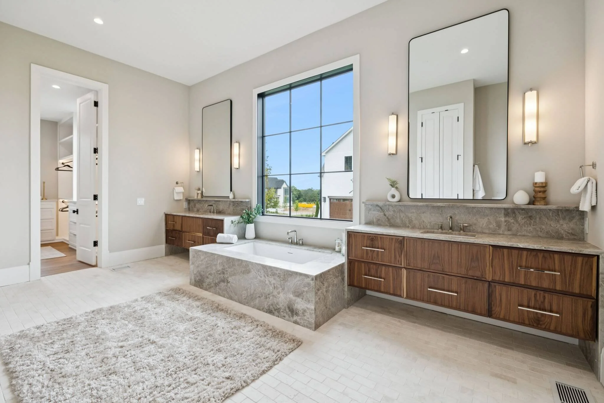 Modern bathroom with large window, bathtub, double vanity with two mirrors, and neutral decor.
