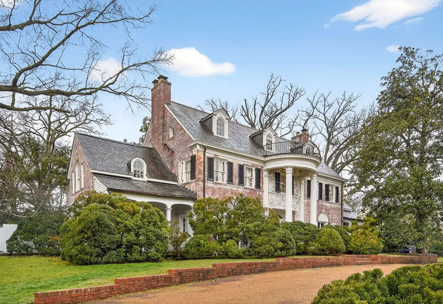 A large white mansion with tall columns at the entrance, surrounded by trees and lit lanterns in a landscaped yard.
