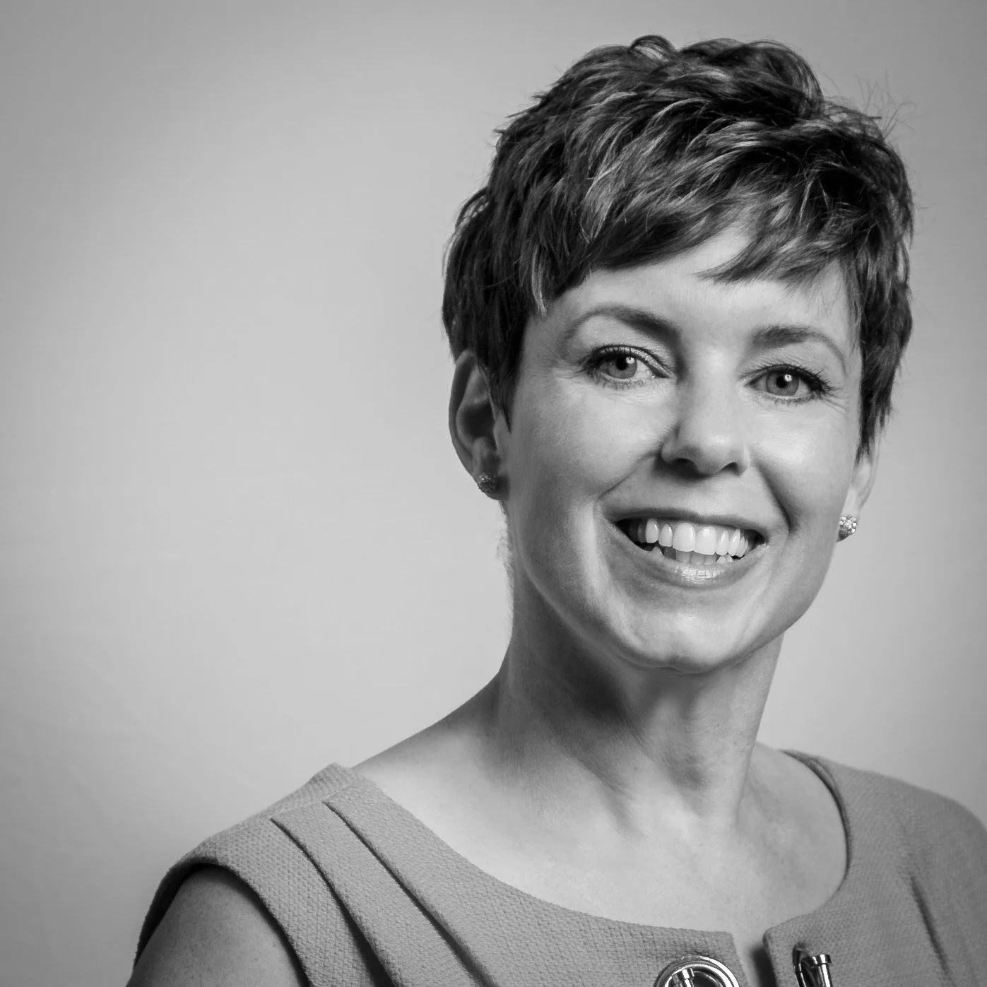 Black and white portrait of a woman with short, styled hair smiling at the camera, wearing a sleeveless top with decorative buttons.