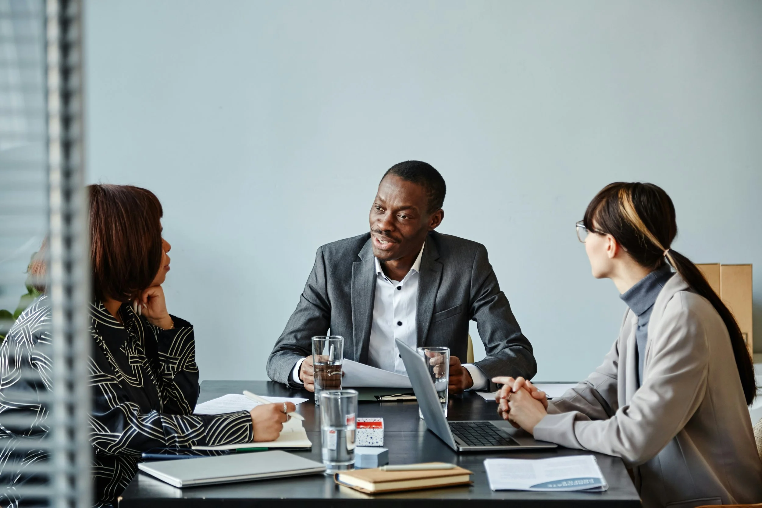 Business meeting with three professionals sitting at a conference table in an office, engaged in discussion.