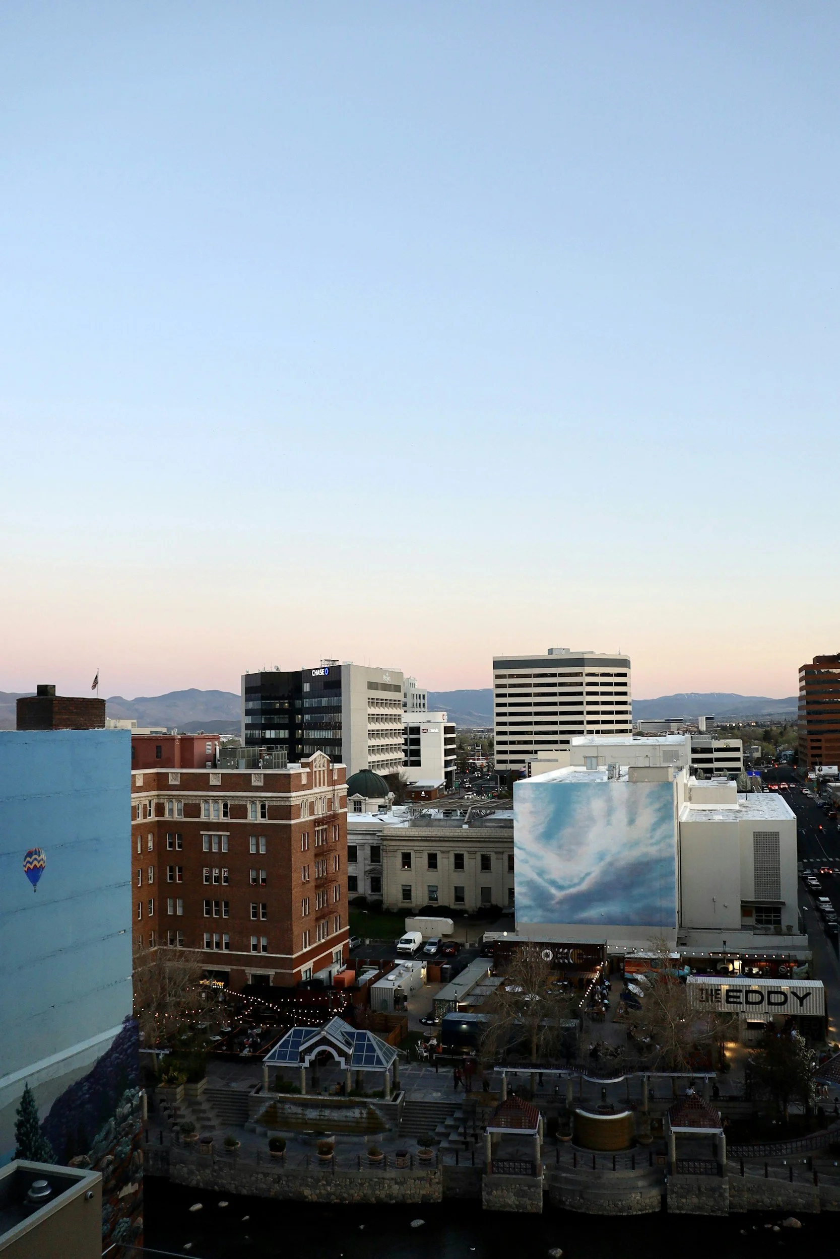Downtown Reno Nevada Cityscape with various buildings, some with murals, under a clear evening sky with mountains in the background.