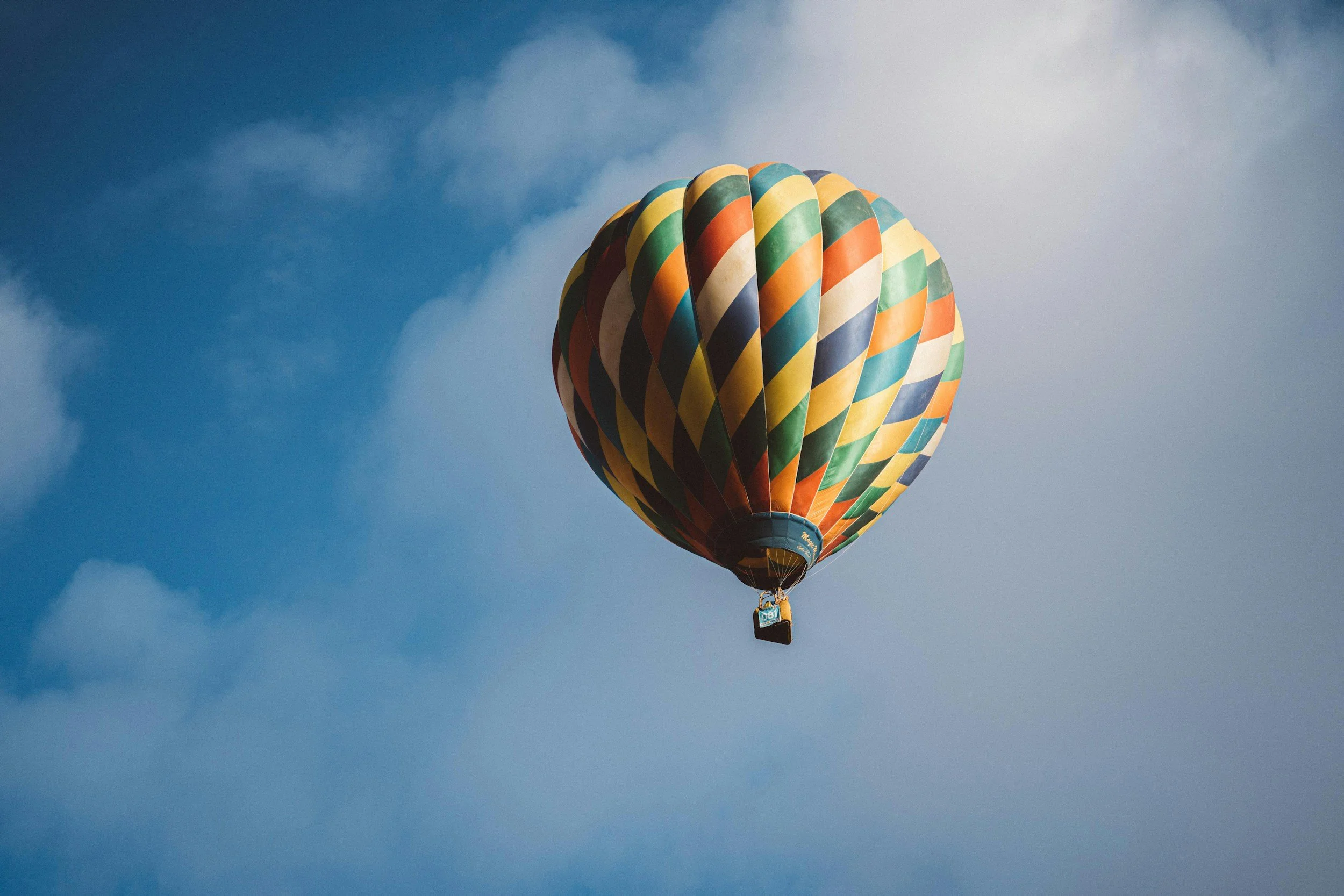 Colorful hot air balloon flying in blue sky above Reno with clouds.