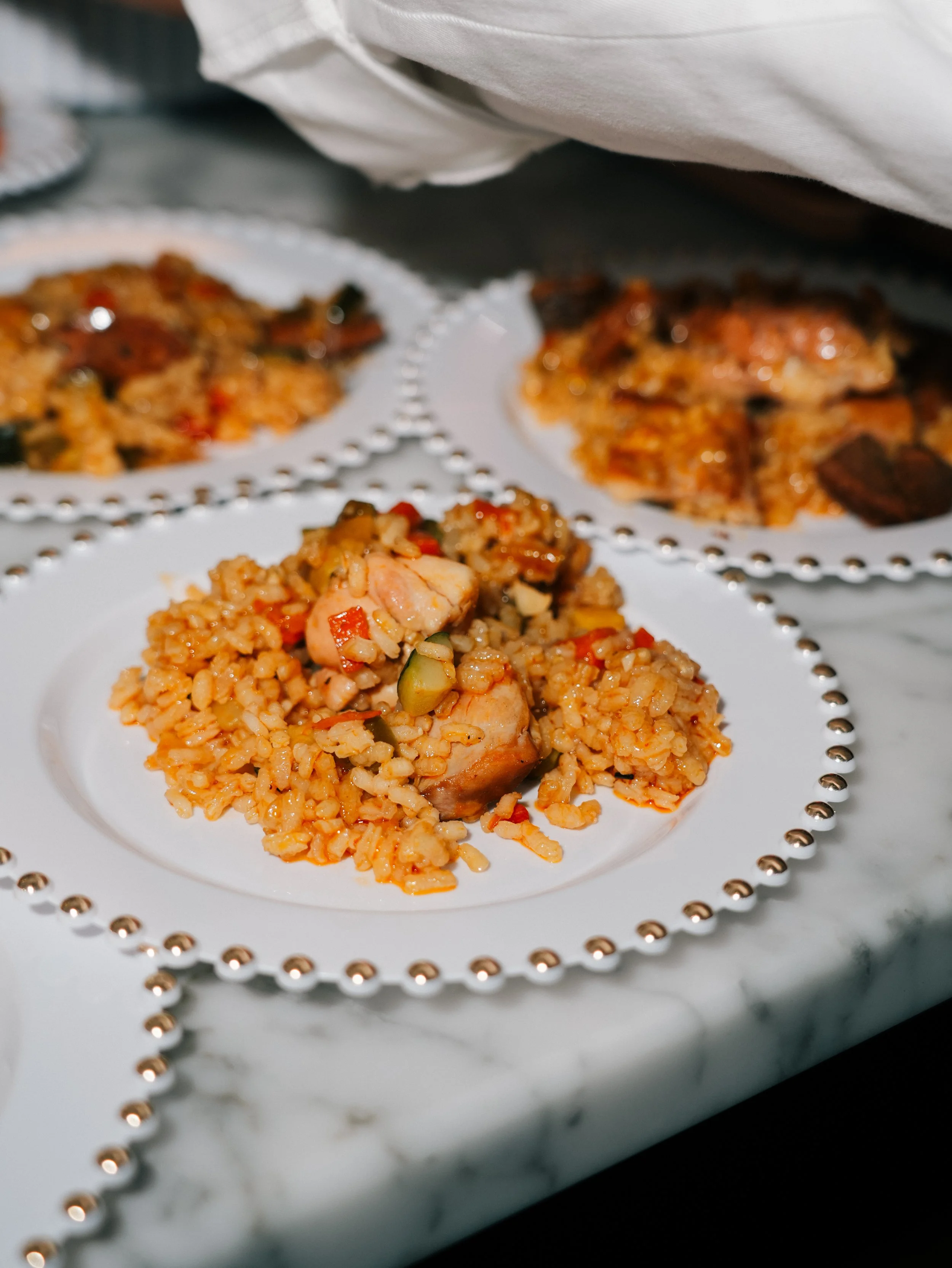 A white plate with fried rice and pieces of chicken, garnished with vegetables, on a marble table.