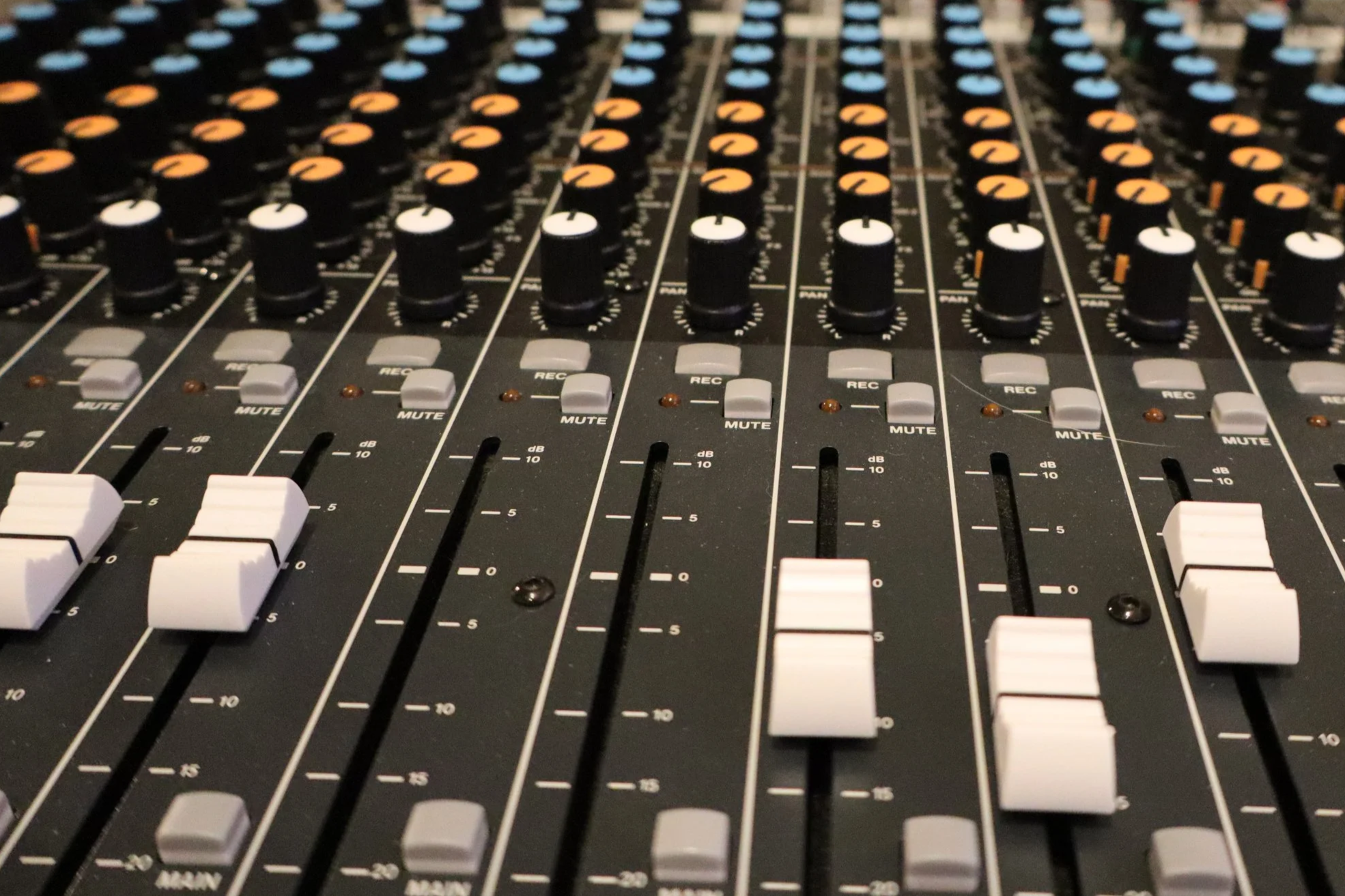 Close-up of an audio mixing console with multiple black and white knobs, faders, and buttons for controlling sound levels and effects.