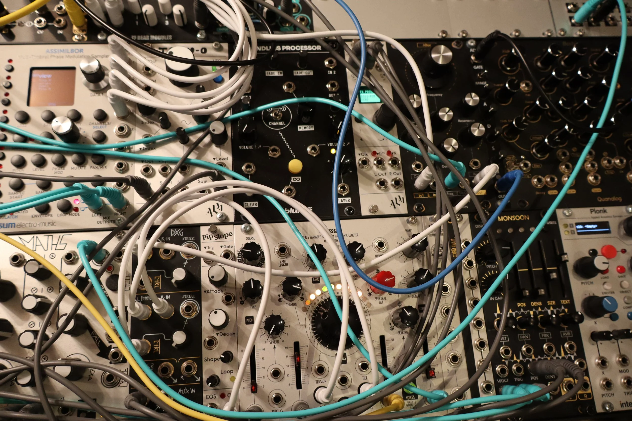 A close-up view of a modular synthesizer with multiple interconnected modules, knobs, switches, and patch cables in various colors.