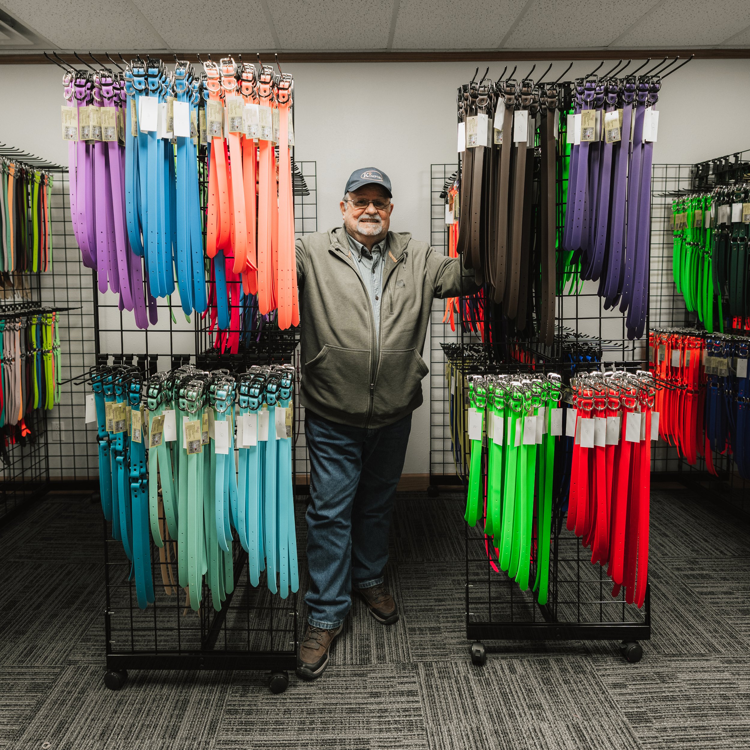 A man with glasses, a cap, and a beard standing in a store aisle with multiple colorful leashes displayed on racks.