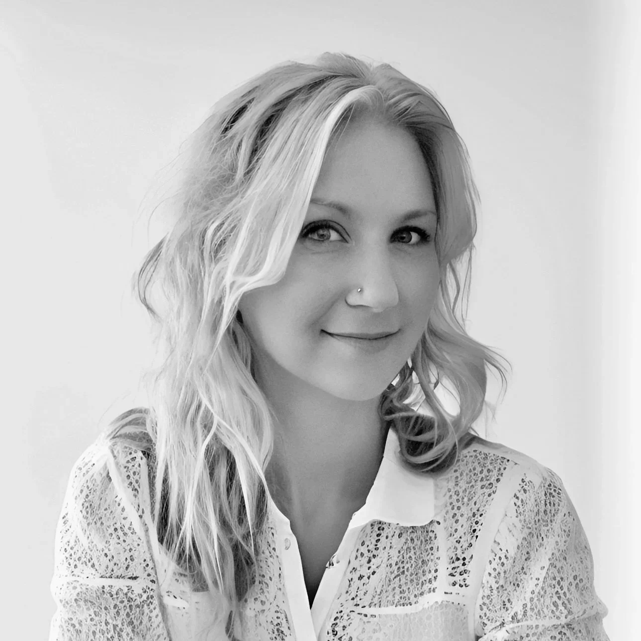Black and white portrait of a woman with wavy blonde hair, wearing a white lace top, smiling softly.
