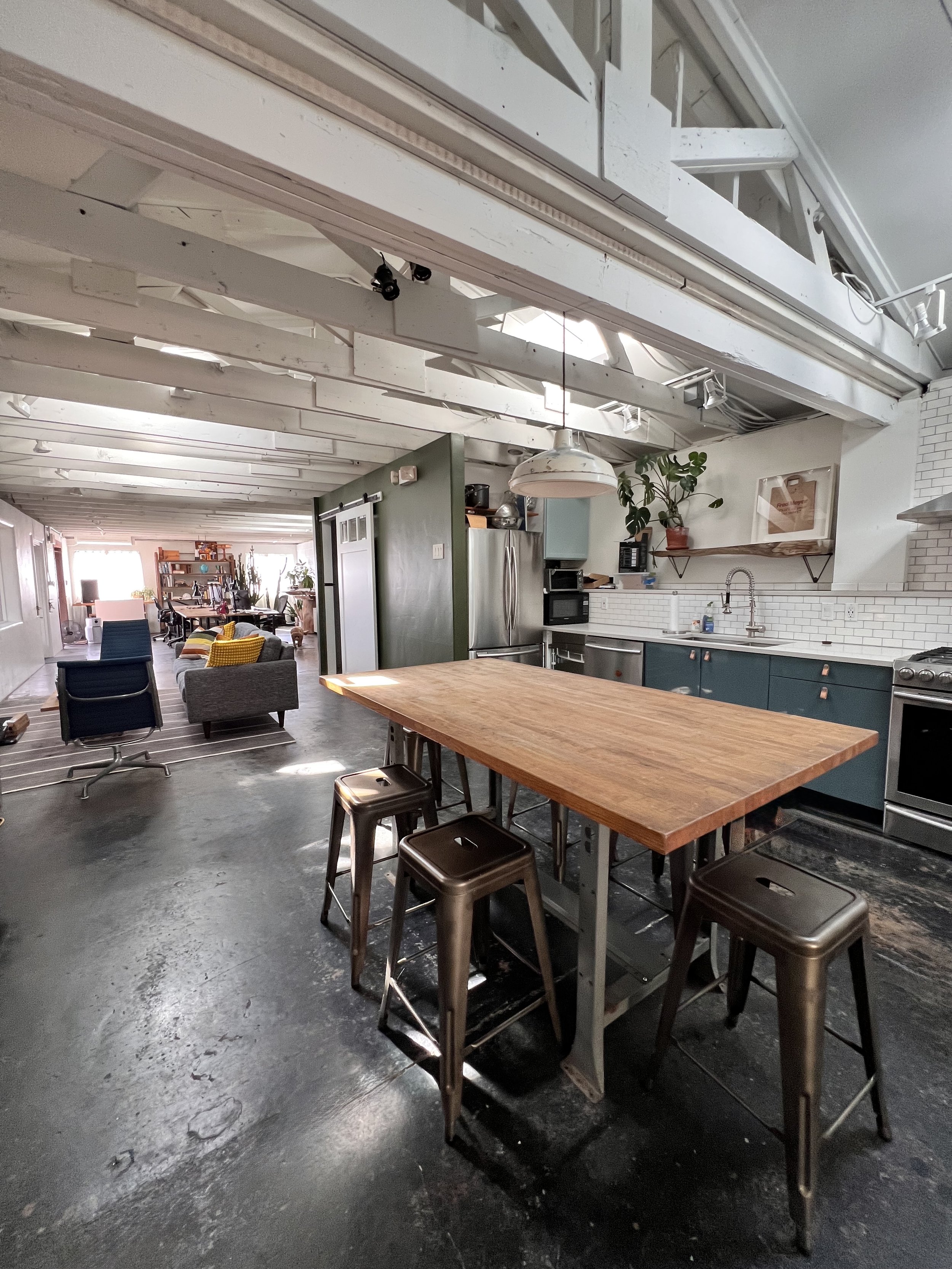 Modern open-concept kitchen with a wooden island counter and three metallic stools, white brick backsplash, stainless steel appliances, and a mix of vintage and industrial decor.
