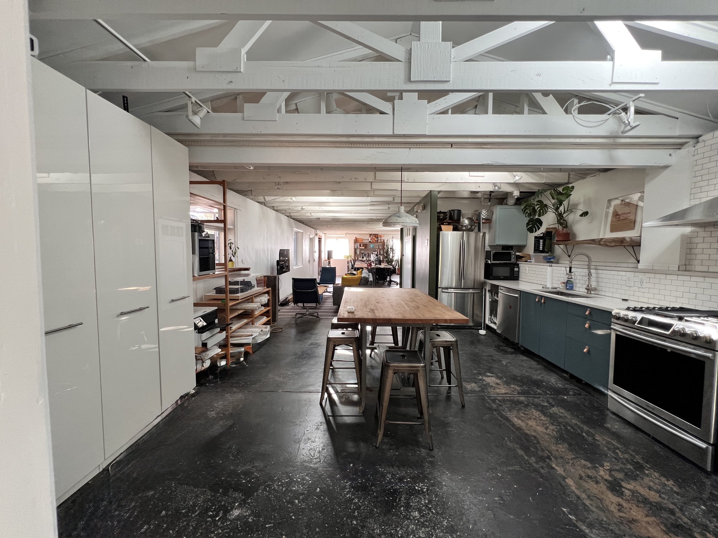 Open-concept kitchen and living area with white cabinetry, stainless steel appliances, a wooden table with stools, and modern decor.